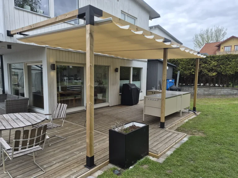 Beige pergolasegel med mittöppning över en uteplats och ett utekök vid huset