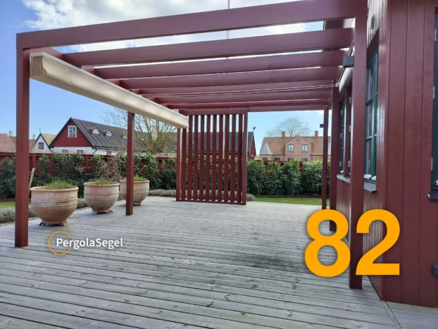 Faluröd pergola i Åhus med beige segel insamlat längst från huset så att fönstren hålls fria