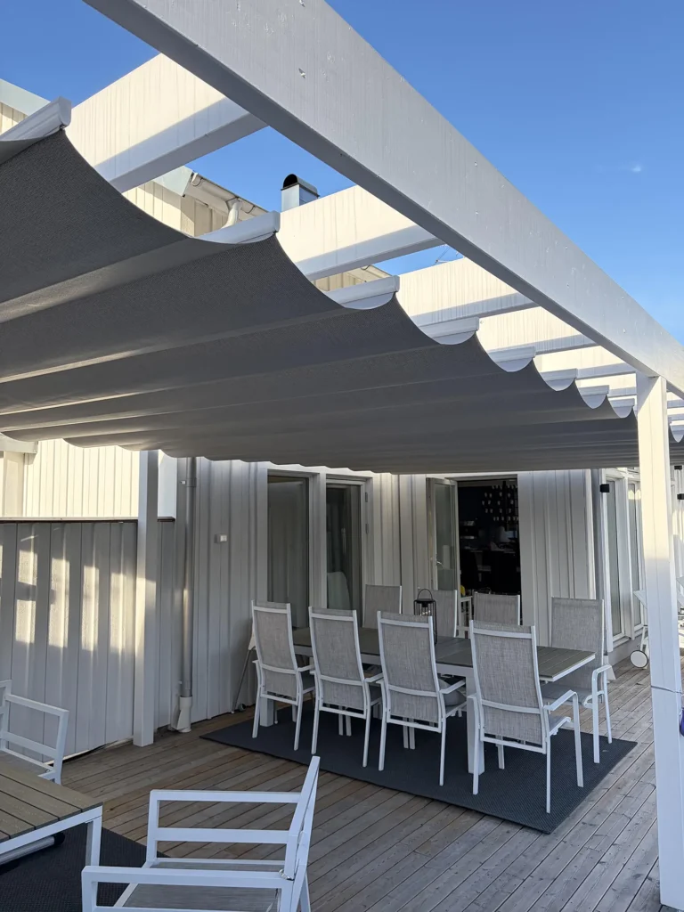 Närbild av en grå pergolamarkis med mittöppning i en vit pergola vid huset