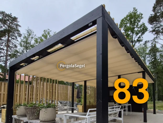 Svart pergola i limträ med beige segeltak över uteplatsens loungemöbler och matplats