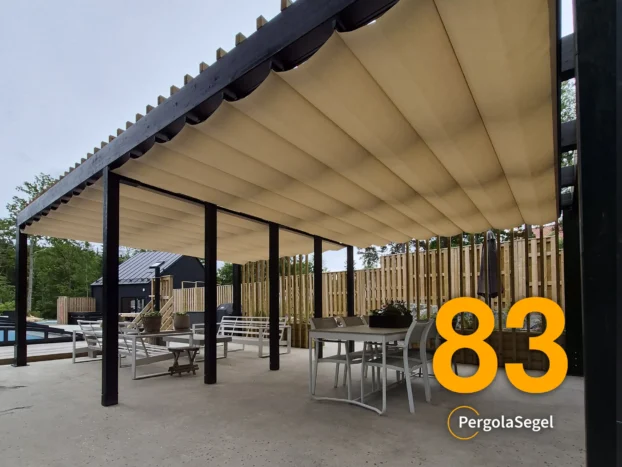 Svart pergola med beige Ferrari W95 duk och träspaljé längs matplatsen