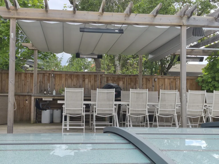 Träpergola med ljusgrå pergolamarkis samlad i mitten över en matplats vid poolen