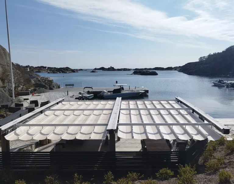 Två ljusa pergolamarkiser med sidoöppning över en havsnära uteplats