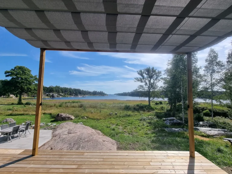 Väggmonterad pergolamarkis med grå duk över en havsnära uteplats