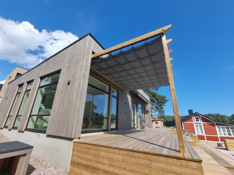Väggmonterad pergolamarkis med grå duk på ett modernt trähus