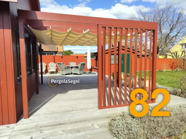 Väggmonterat pergolasegel med beige duk över uteplatsen och faluröd spaljé vid pergolans ytterkant